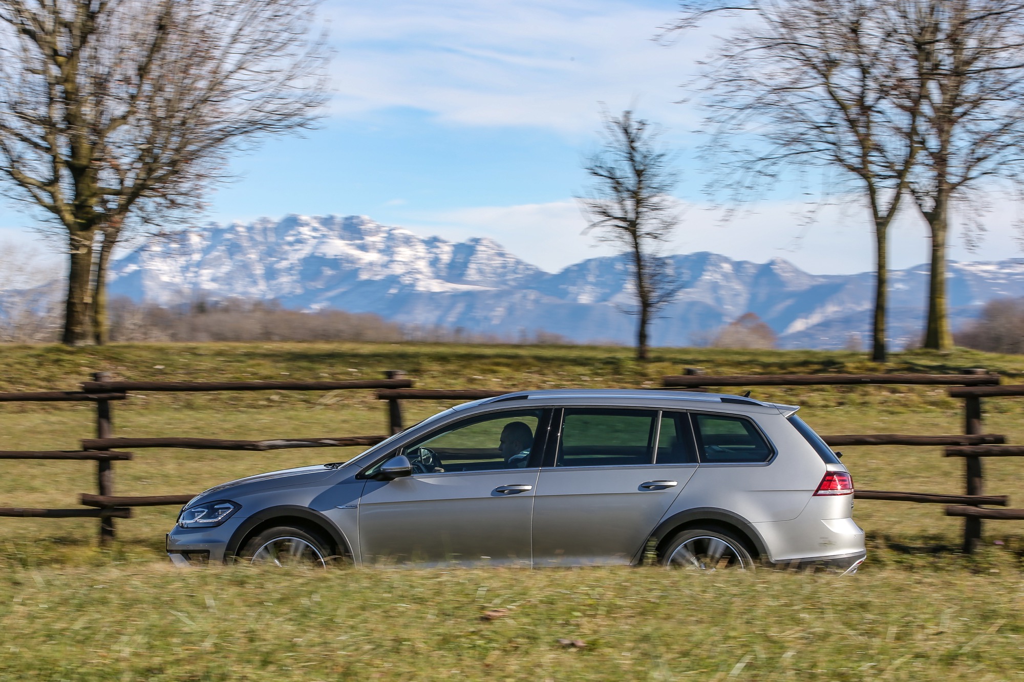 Volkswagen Golf Alltrack laterale in movimento grigia con dietro montagne su strada
