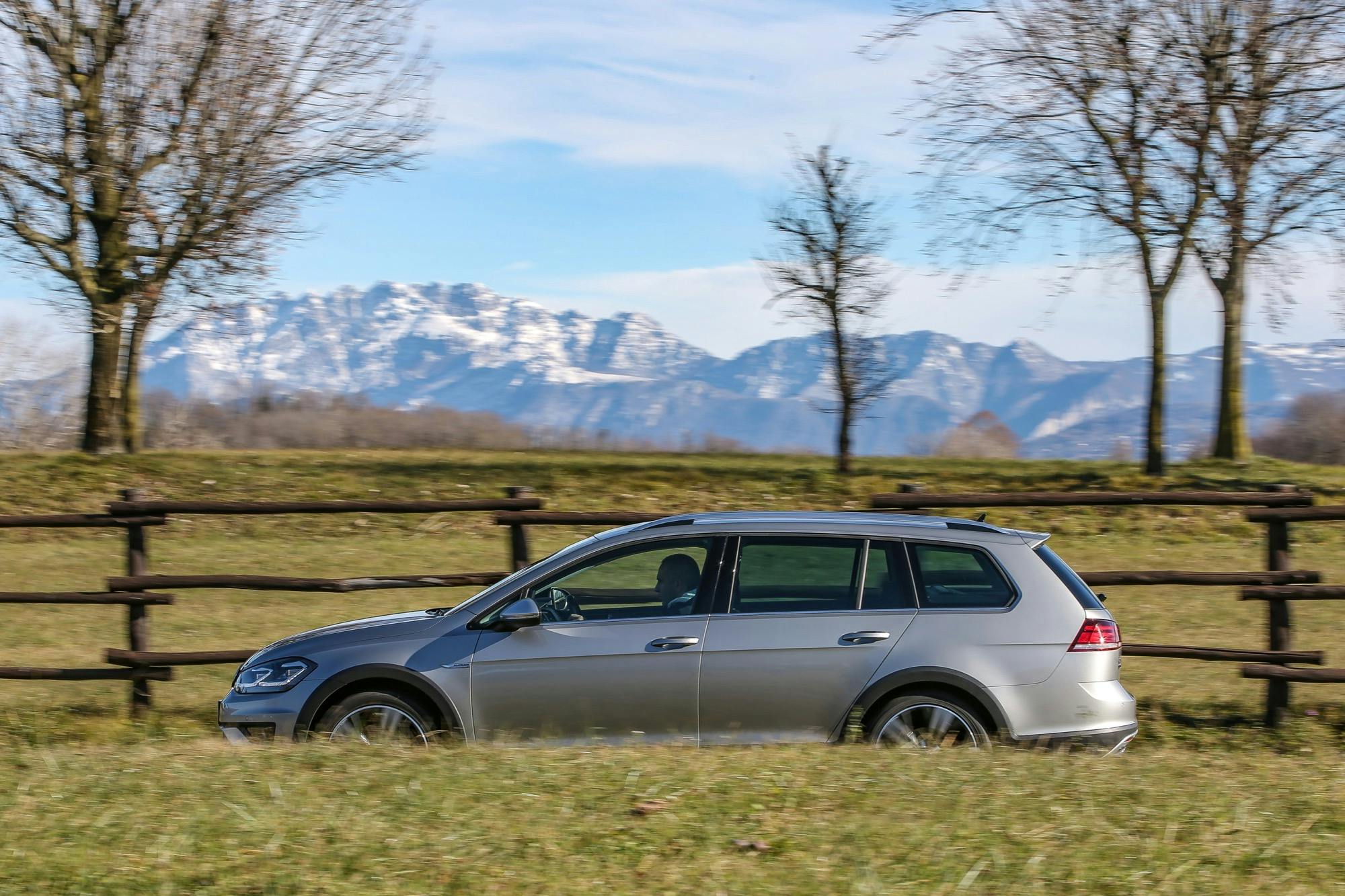 Volkswagen Golf Alltrack laterale in movimento grigia con dietro montagne su strada
