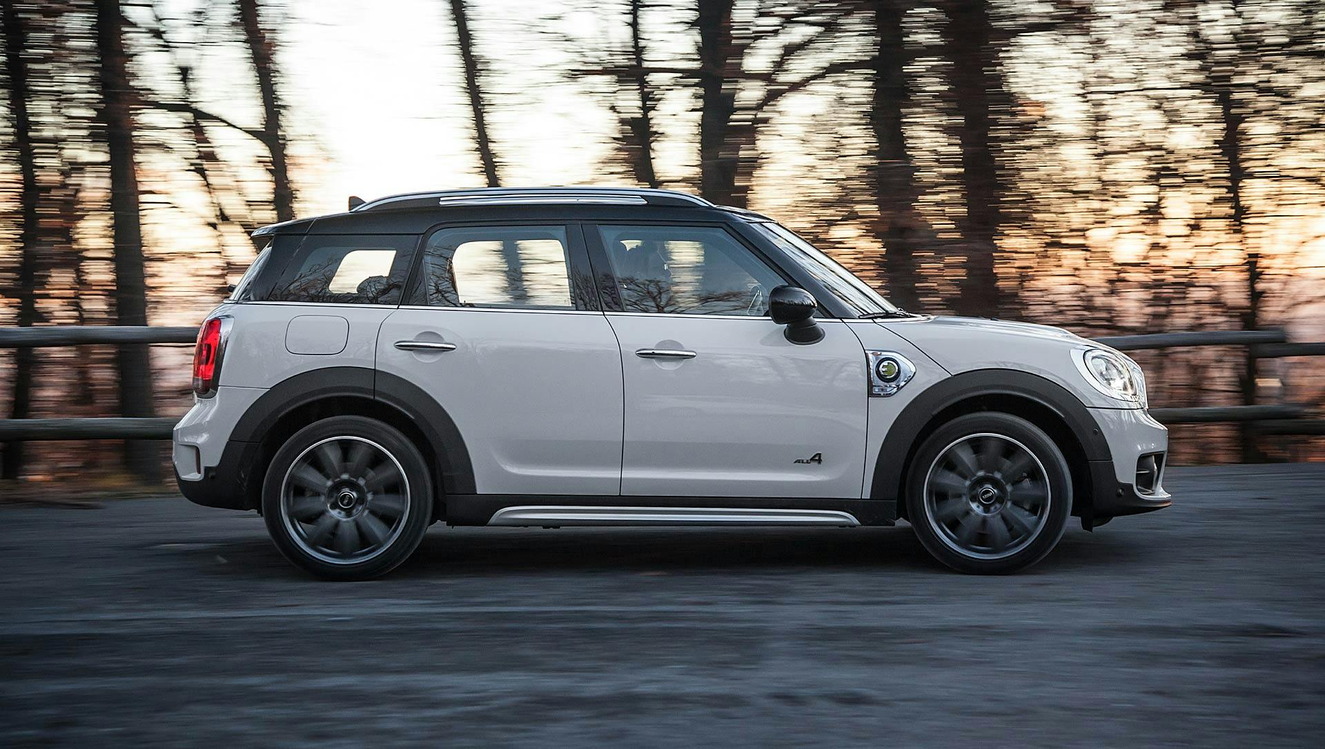 Mini Cooper Countryman SE bianca in curva con sfondo di alberi e tramonto