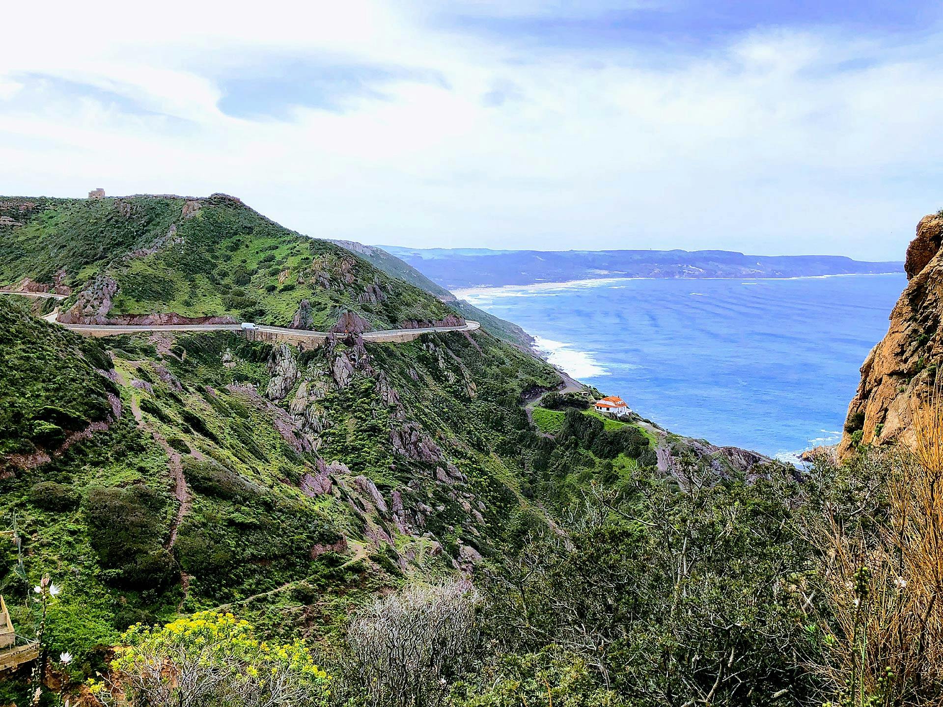 Vista dall'alto di una strada tortuosa della Sardegna del Sud, sullo sfondo si scorge il mare