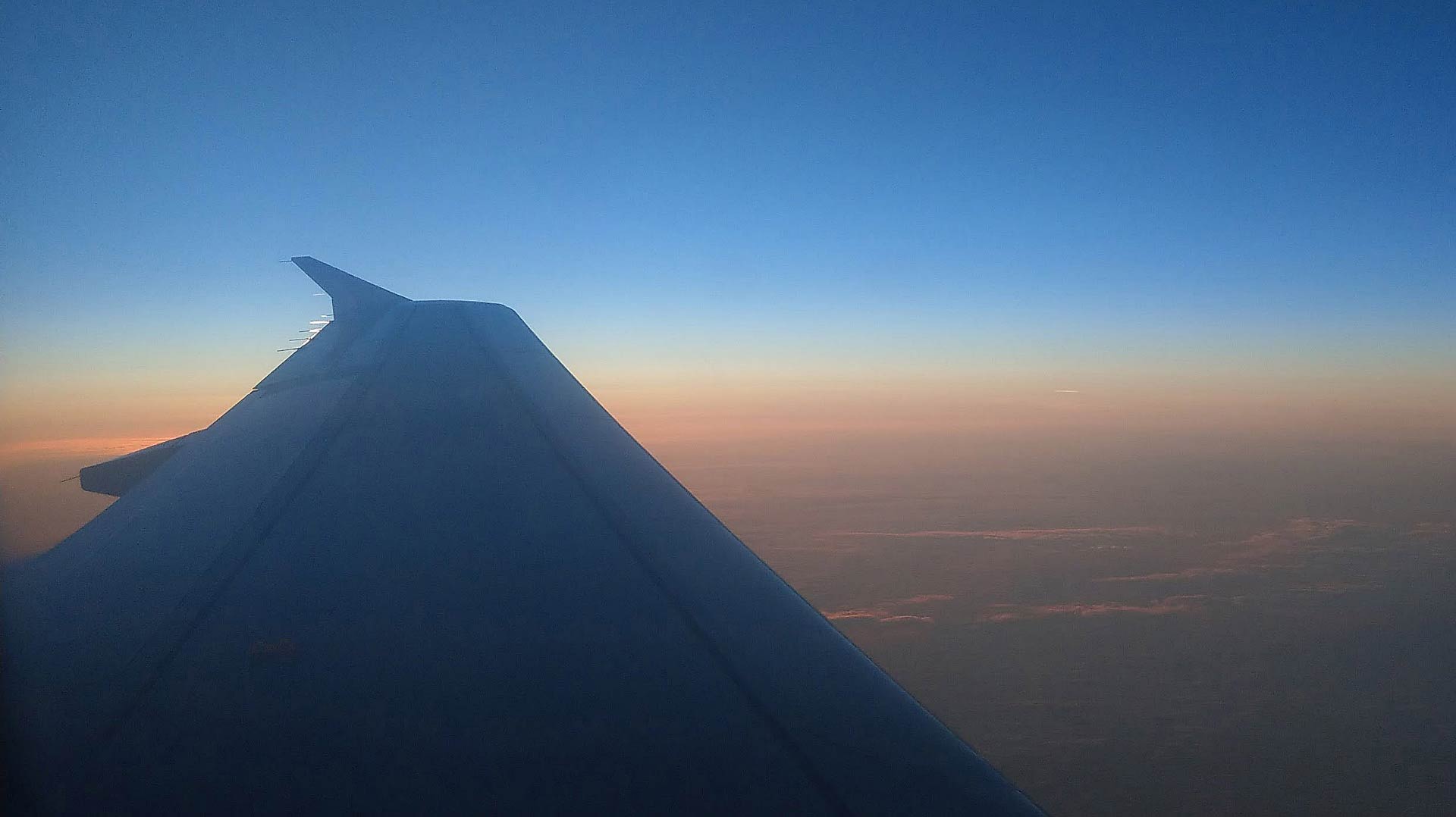 In volo si apprezza lo spettacolare cielo colorato dal tramonto rosso arancio con sfumature verdi