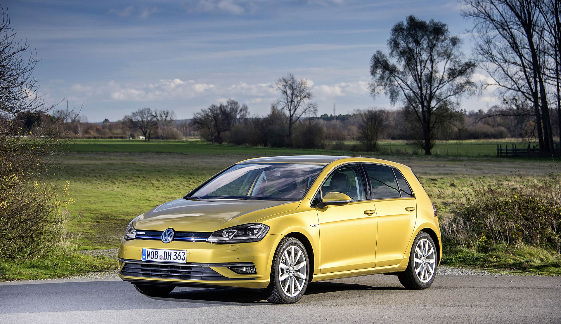 Vw Golf gialla davanti a un campo con alberi