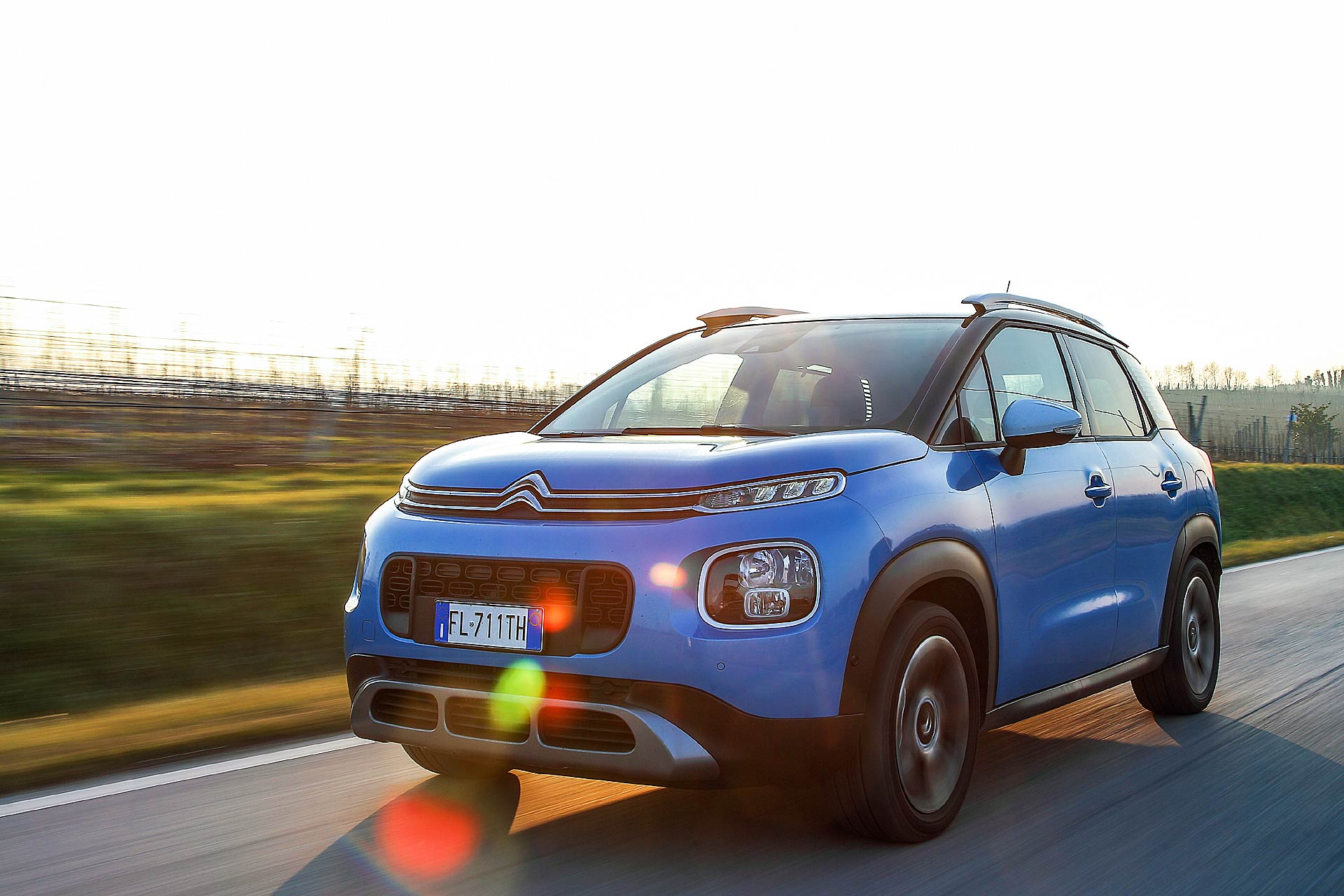 Citroën C3 Aircross azzurra corre nelle verdi campagne con riflesso del sole