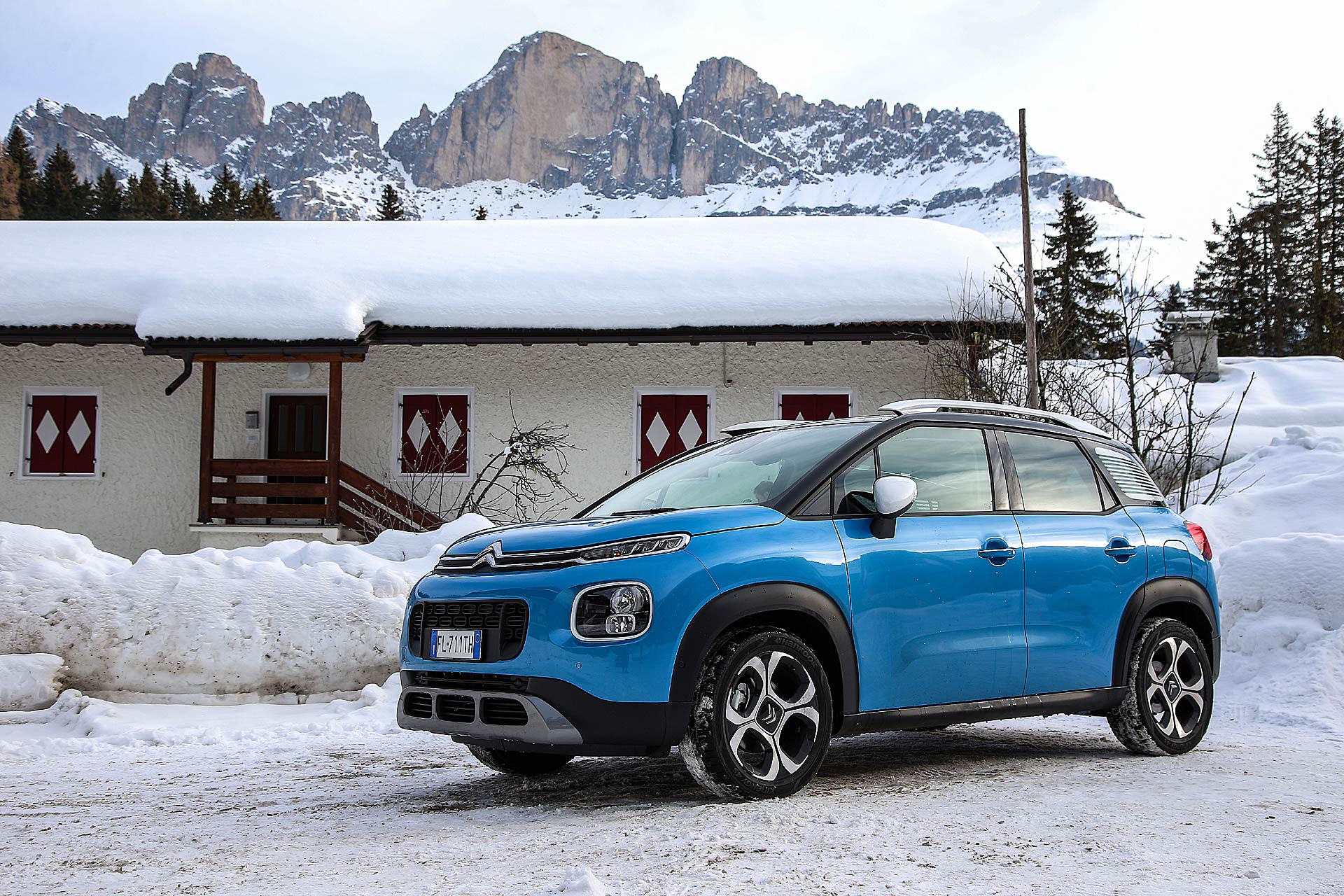 Citroën C3 Aircross azzurra sulla neve statica con casa dietro