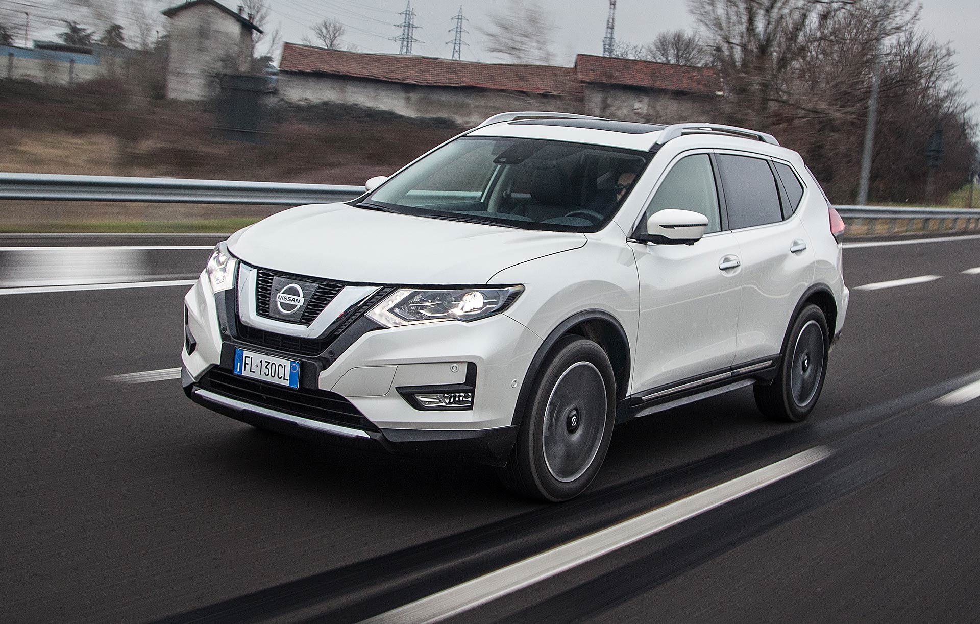 Nissan X-Trail 1.6 dCi 130 CVT 2WD Tekna bianca in autostrada con dietro una cascina