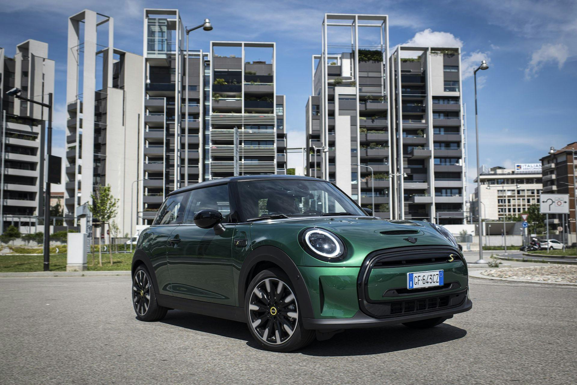 Mini Cooper SE elettrica, di colore verde, ripresa frontalmente di tre quarti con edifici sullo sfondo