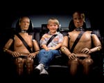 bambino seduto sul divano di una auto con due manichini da crash test