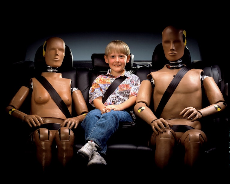 bambino seduto sul divano di una auto con due manichini da crash test